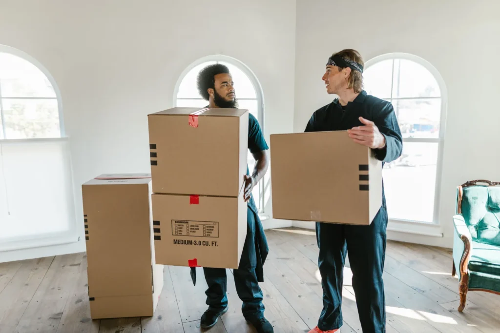 Zwei Mitarbeiter tragen Kartons aus einem leergeräumten Zimmer