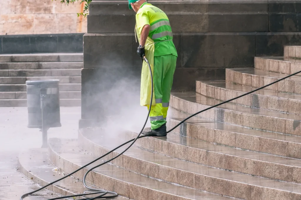 Mitarbeiter in Warnschutzkleidung reinigt eine Gebäudetreppe mit dem Hochdruckreiniger