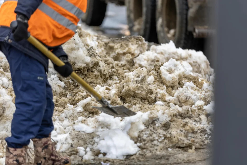 Mitarbeiter in Warnkleidung räumt Schnee von einer Verkehrsfläche